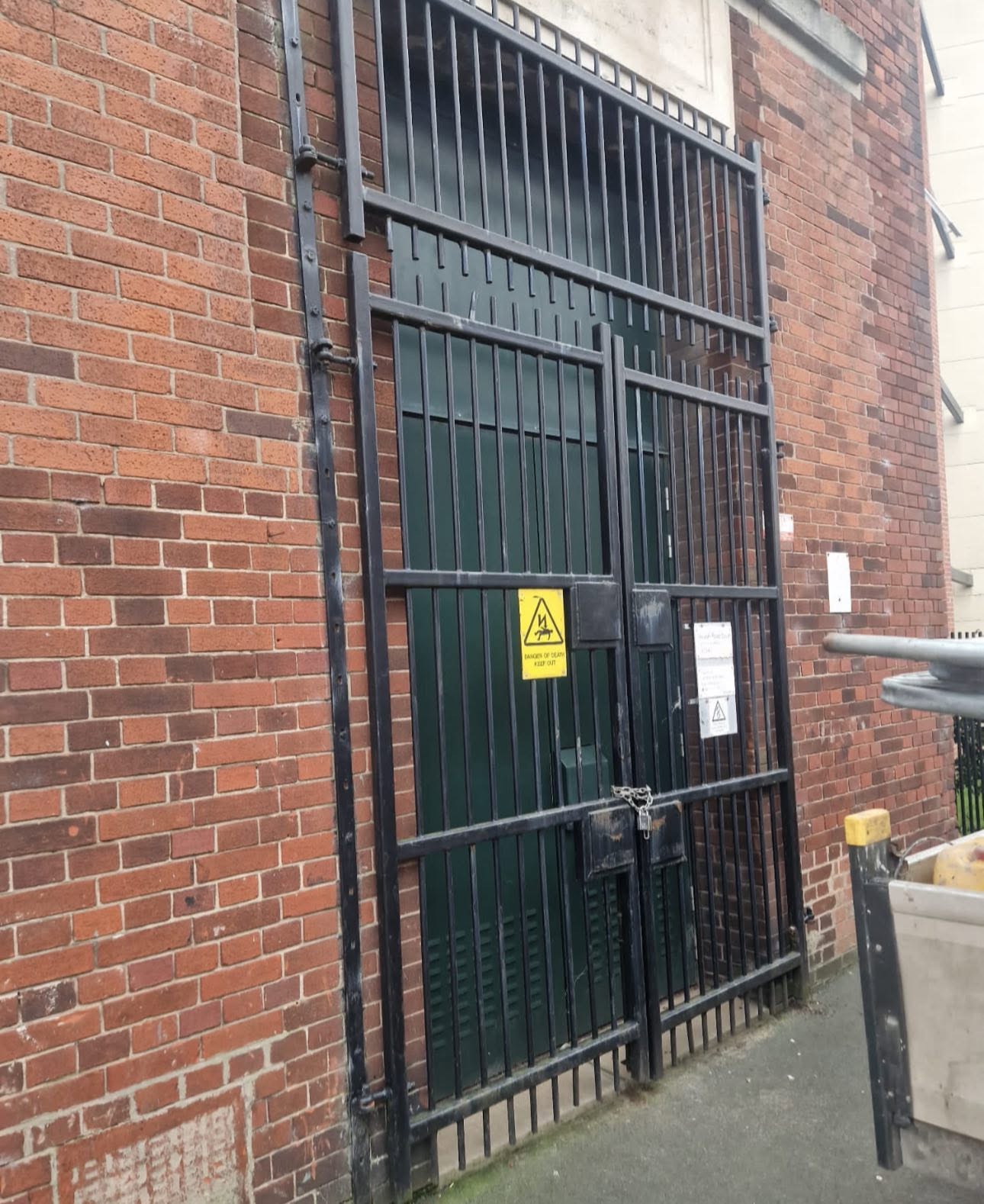 Tall black powder-coated vertical steel bar gates protecting a substation door in a red brick building