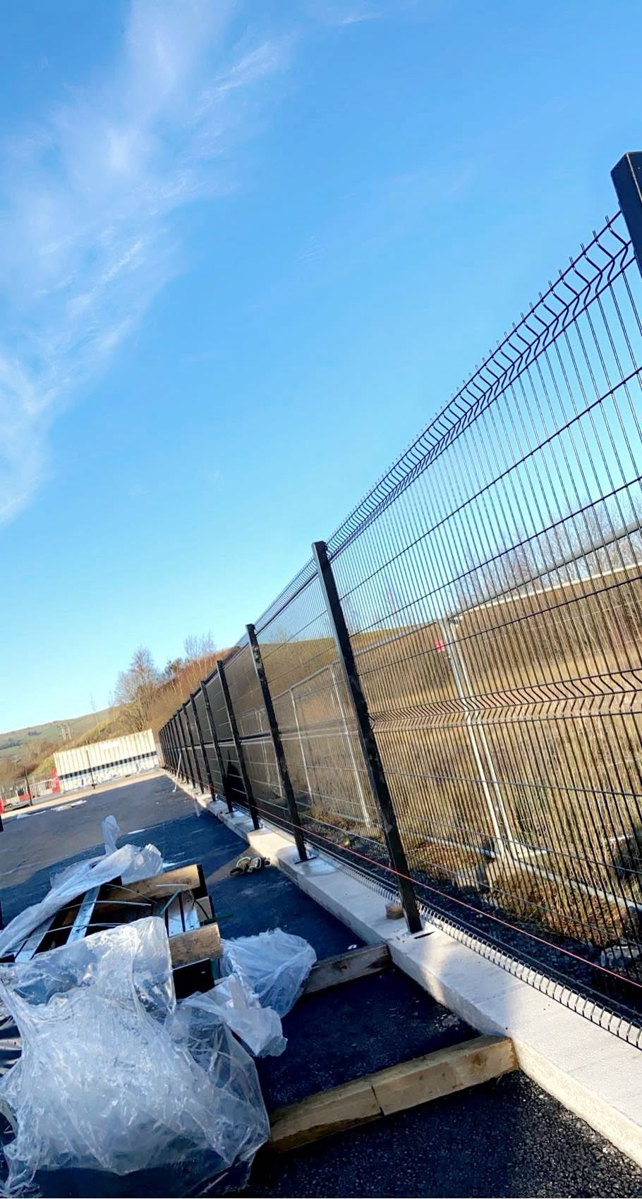 Black powder-coated V-mesh security fencing on concrete gravel boards along a commercial yard