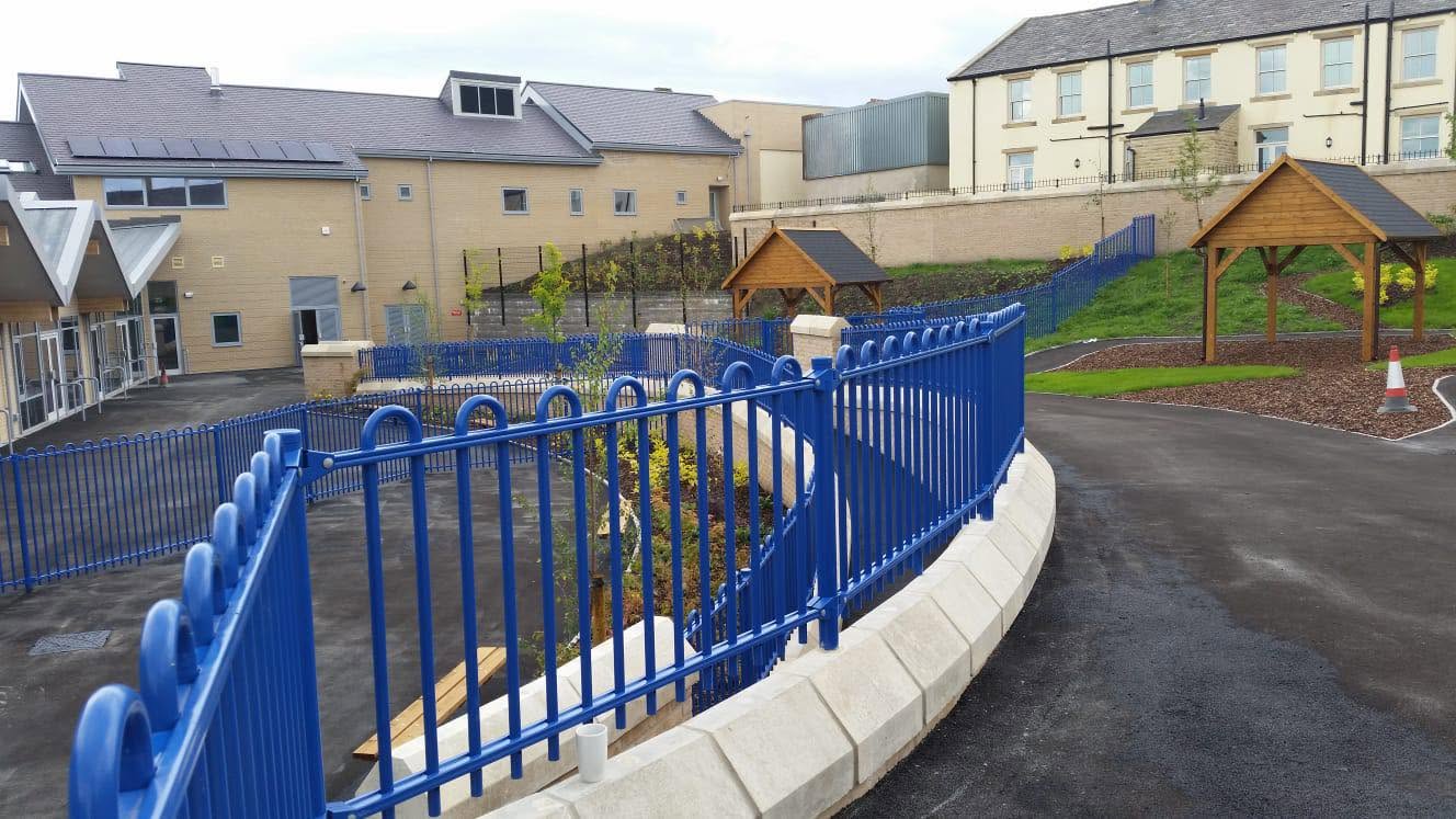 Blue powder-coated bow-top railings installed around a school and community building