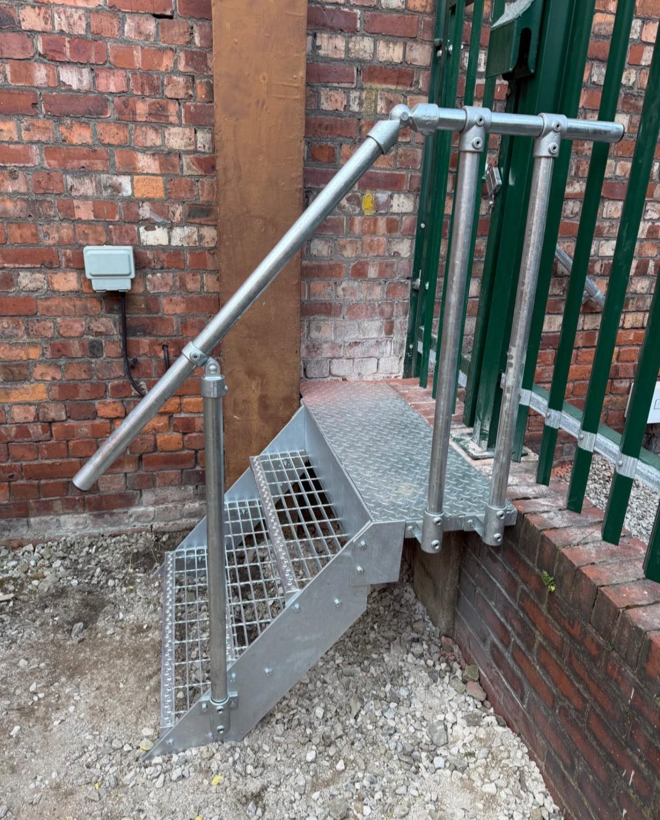 Compact galvanised steel access steps with tubular handrail against a brick wall