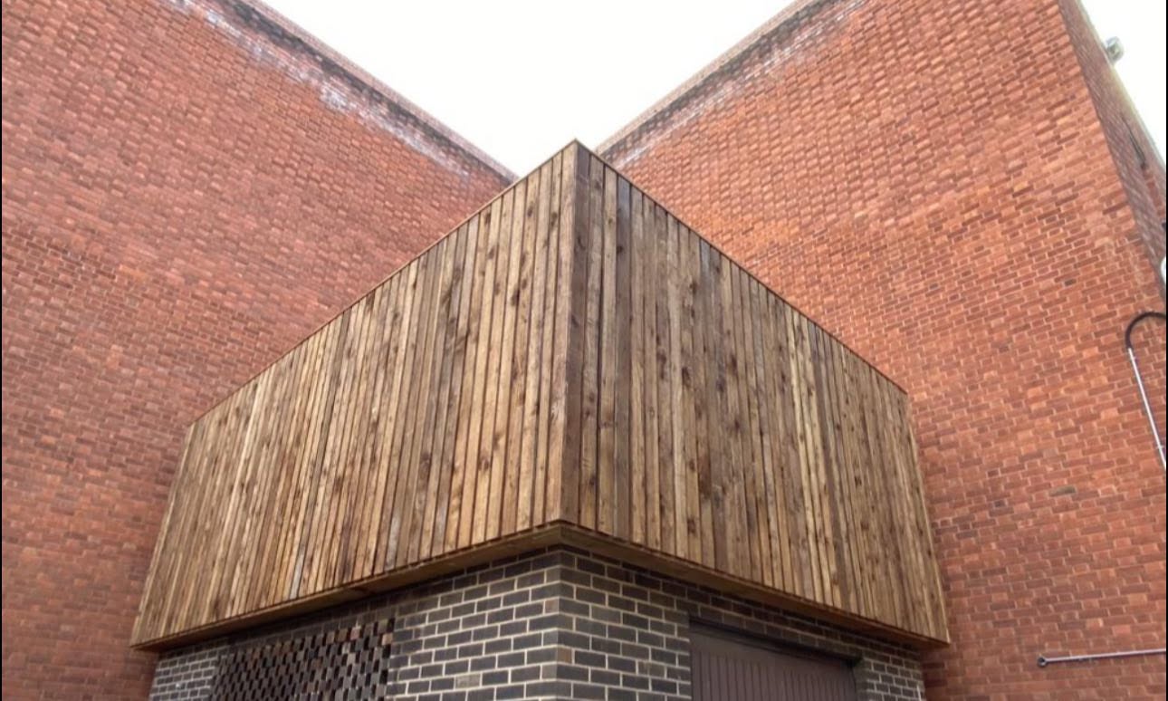 Bespoke timber-clad screen wrapping the corner of a red brick industrial building