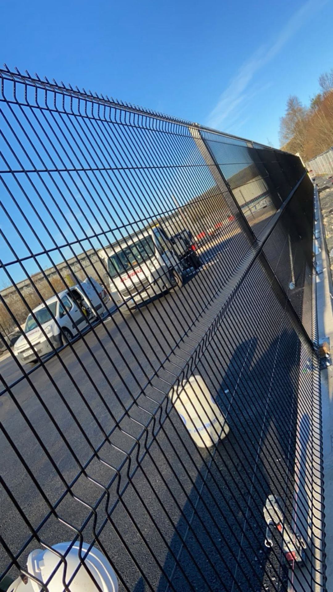 Angled view of black powder-coated V-mesh security fencing around a commercial vehicle yard