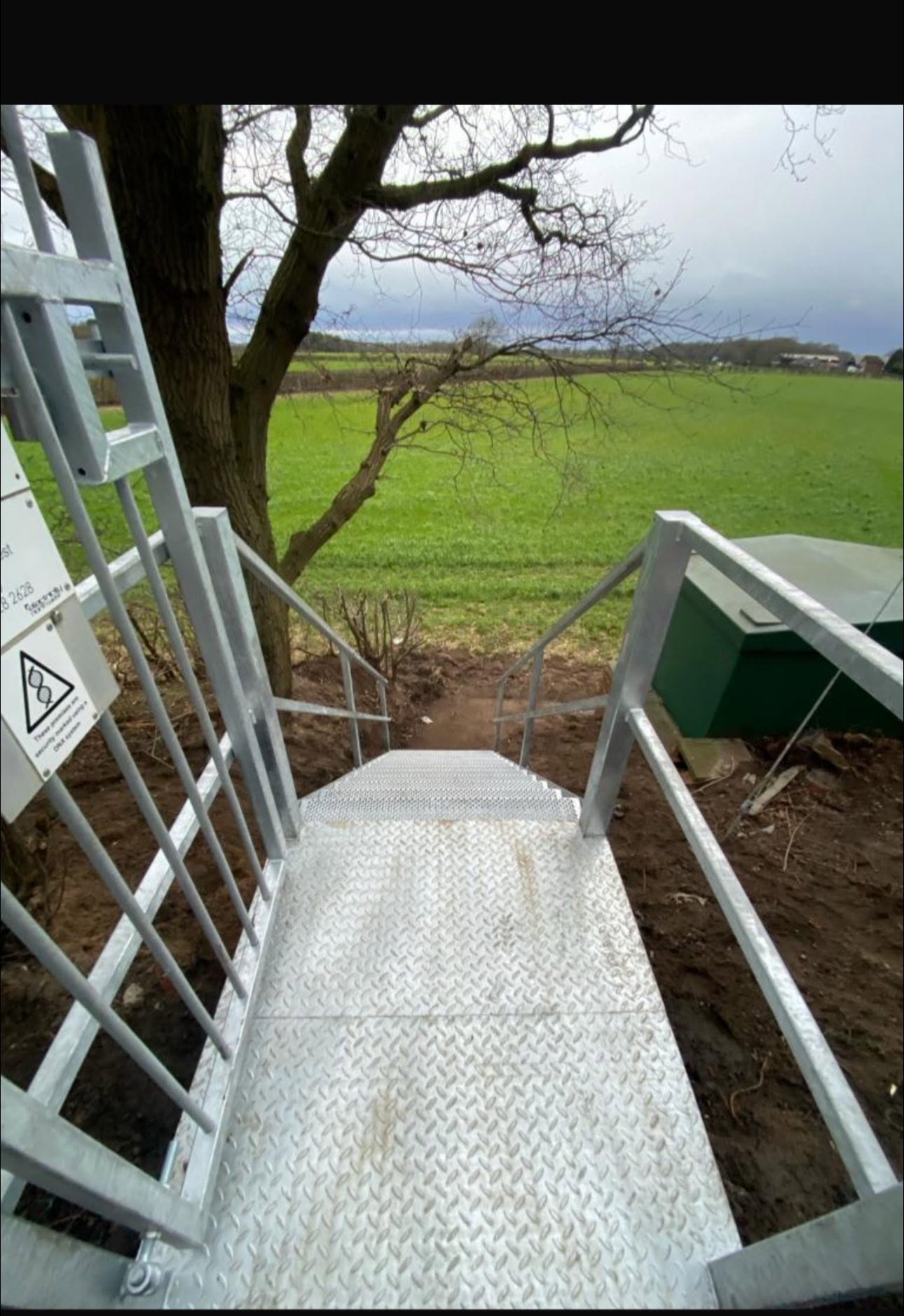 View down a galvanised steel platform staircase overlooking farmland